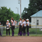 Softball team in huddle by fence in outfield