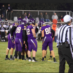 Football players on field in huddle with referee close by